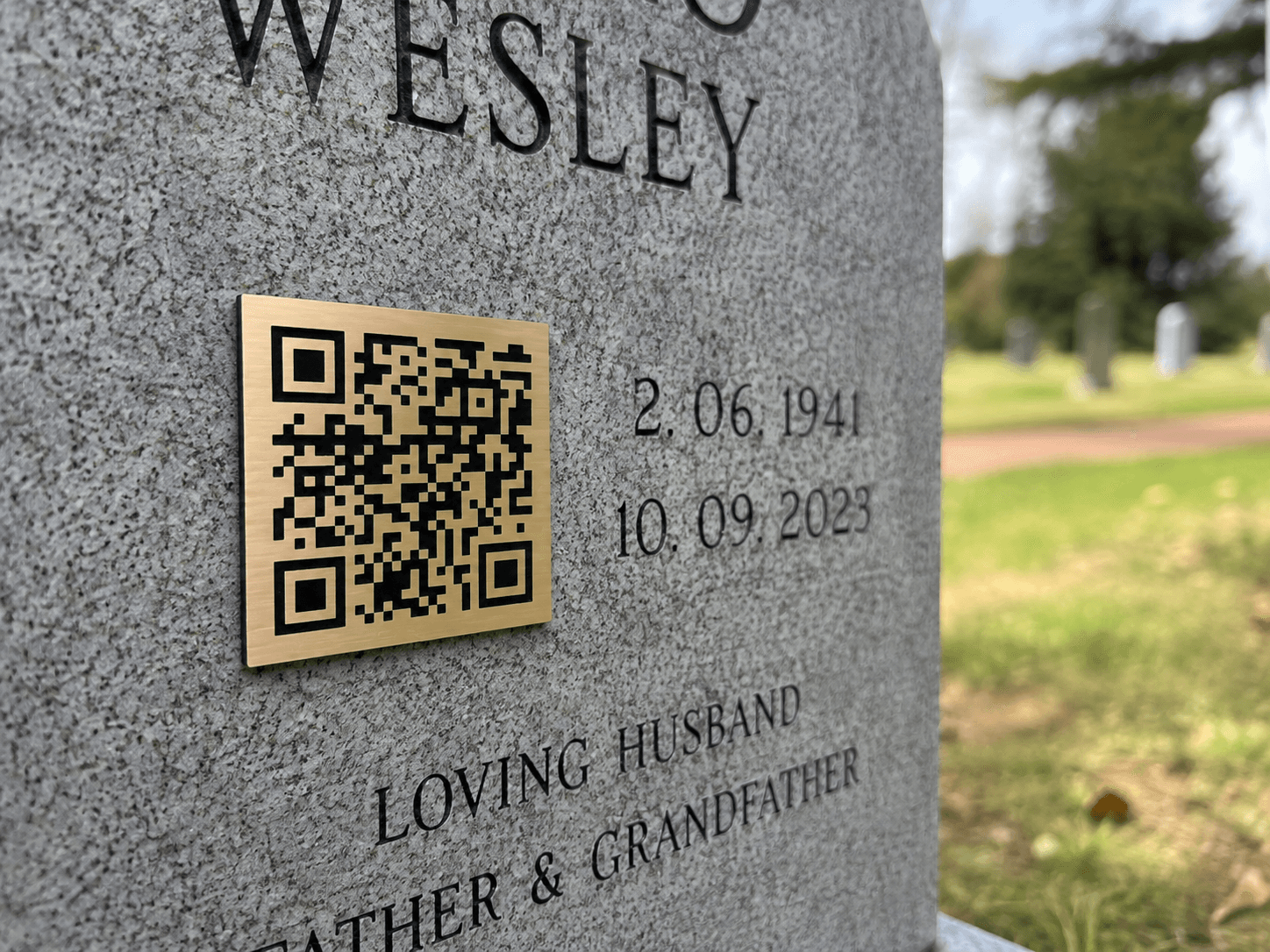 A gold QR plaque engraved and fitted onto a headstone, next to the dates and inscription